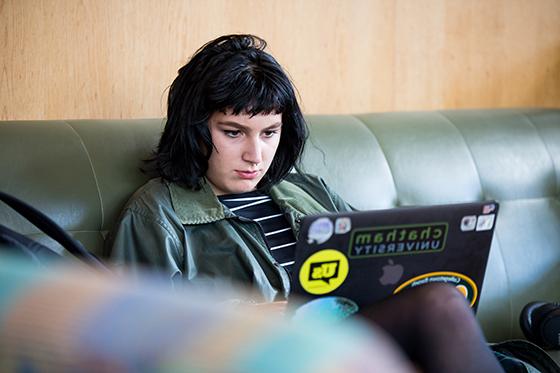 Photo of a Chatham University student sitting on a leather couch, working on her laptop. 